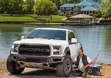 A white Ford car with Hercules Tires in front of a fisherman and a lake. 