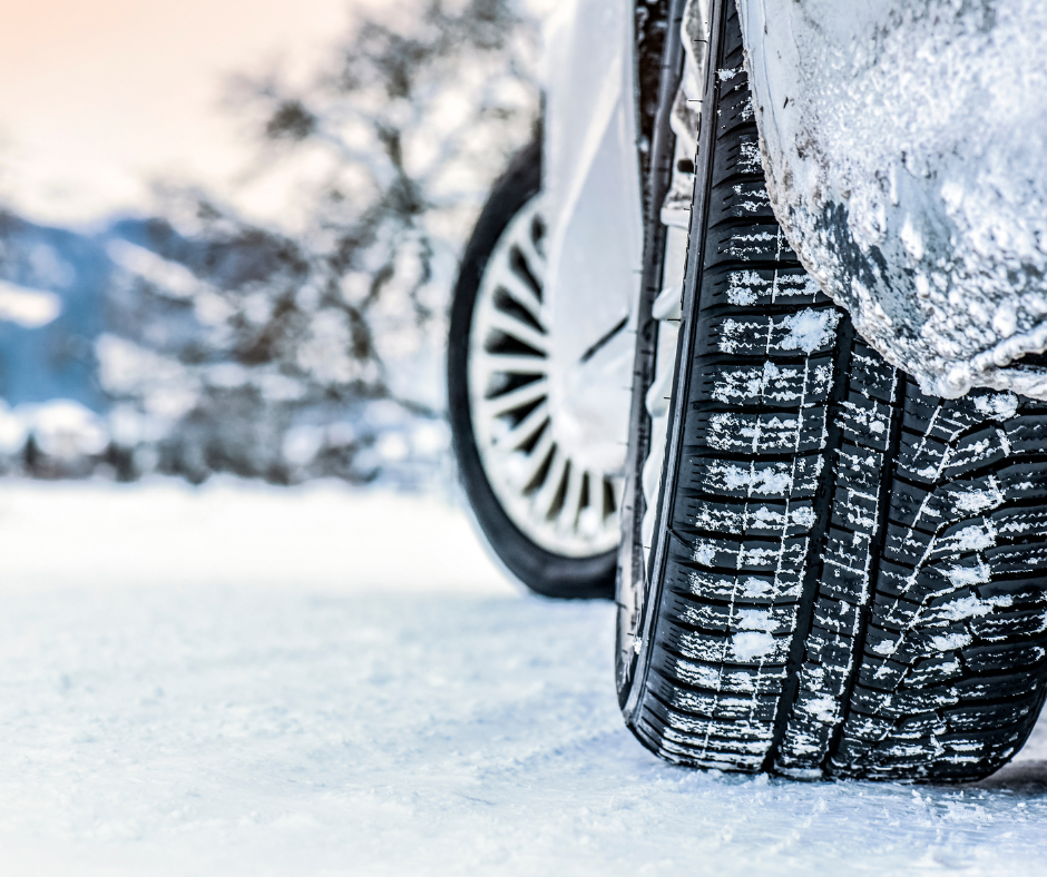 Close-up of a car tire driving on a snow-covered road, showing the tread pattern and snow stuck in the tire.