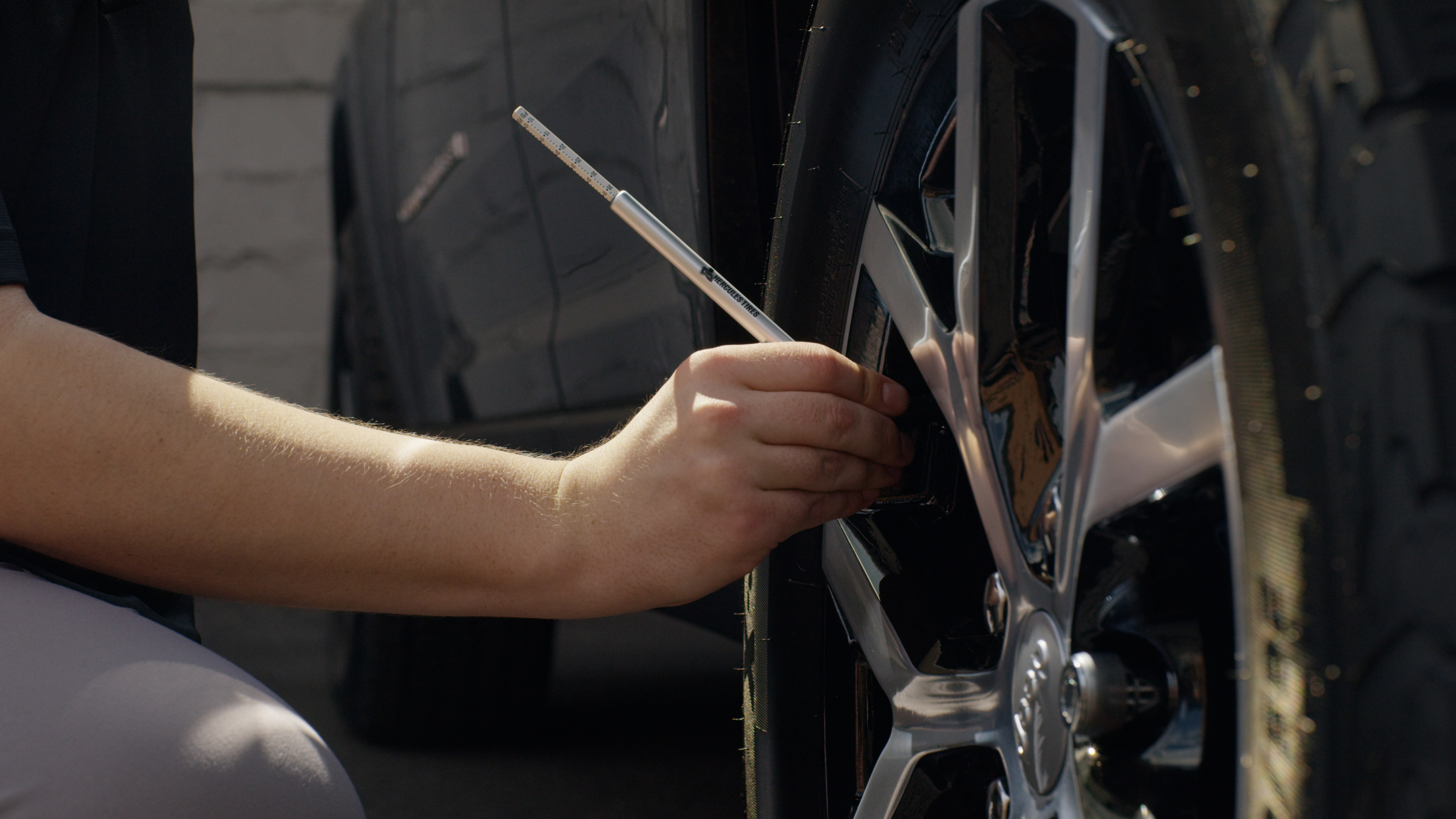 Person checking tire pressure using a gauge, holding the tool against the valve stem of a car tire.