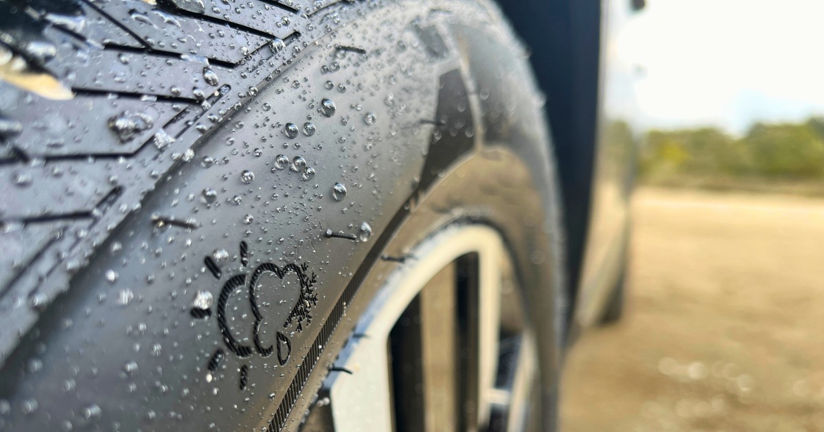Close-up of a tire with water droplets on its surface, showing a three-peak mountain snowflake certification symbol embossed on the sidewall, indicating suitability for different weather conditions.