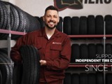 A white male independent tire dealer holds a Hercules Tire in his showroom. The text in the corner says "Supporting independent tire dealers since 1952."
